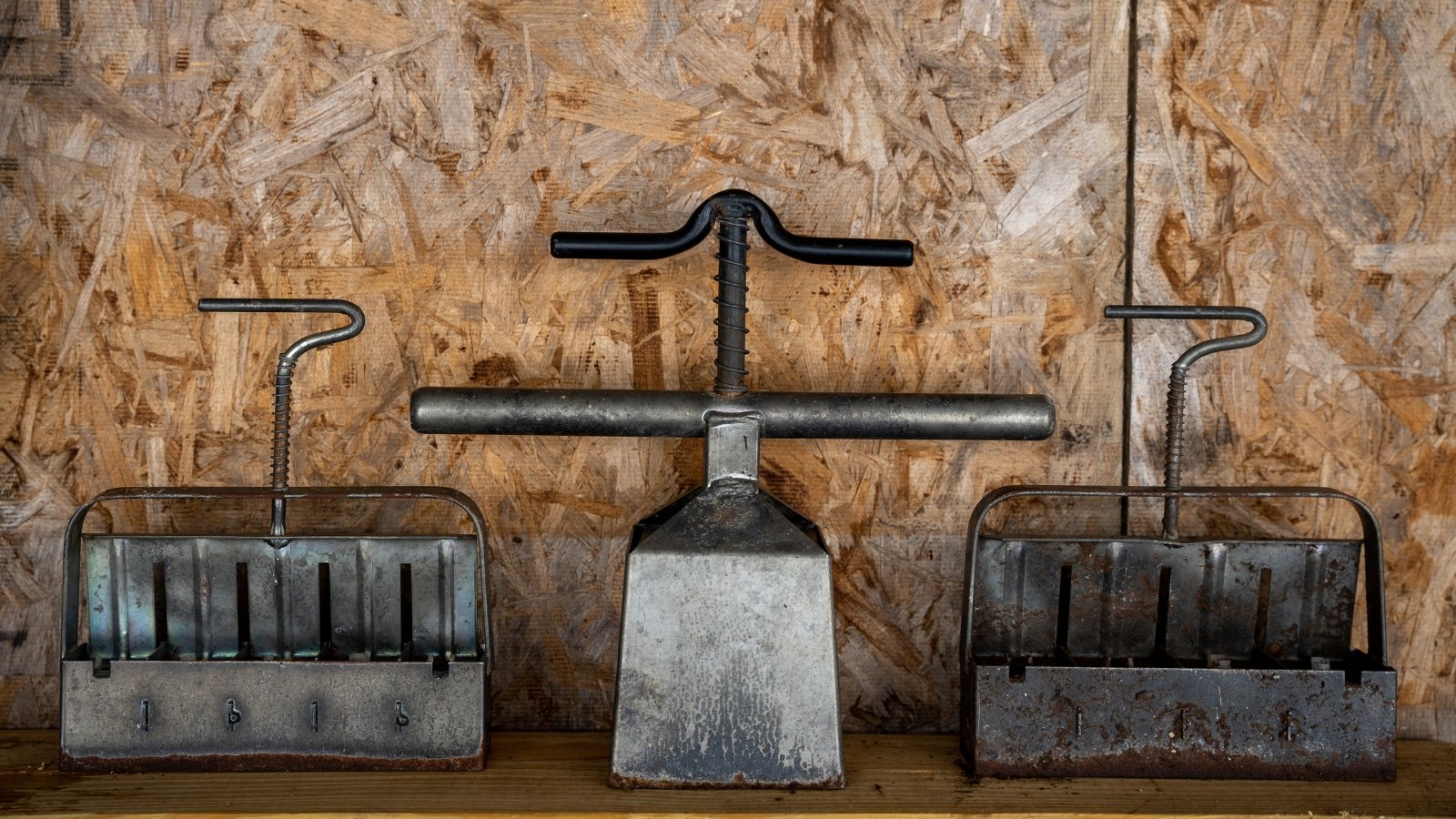 Various tools, including metal presses and a compacting device, are displayed neatly against a wooden backdrop, creating a rustic, organized presentation of planting instruments in a functional workspace.