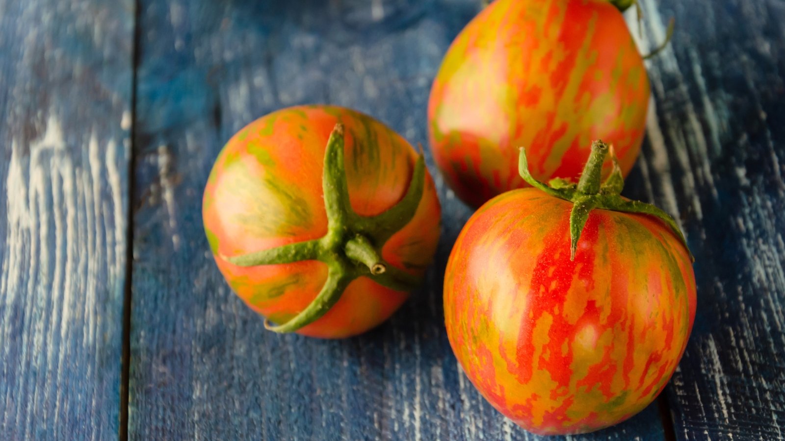 Striped red and yellow tomatoes rest on a rustic wooden surface, showcasing their glossy skin and round shape.
