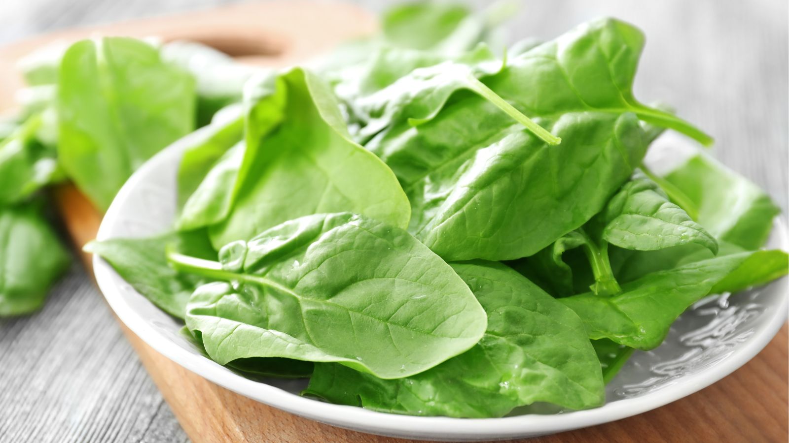 A plate of Lavewa leaves appearing bright green on a wooden surface with other leaves in the background