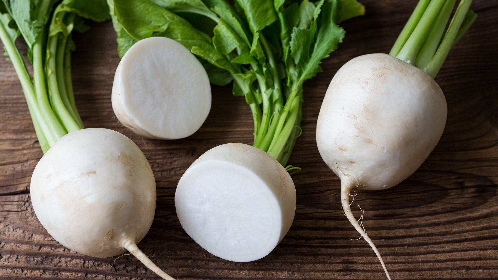 An overhead and close-up shot of several harvested and sliced Seven Top root crops, all placed on a wooden surface indoors